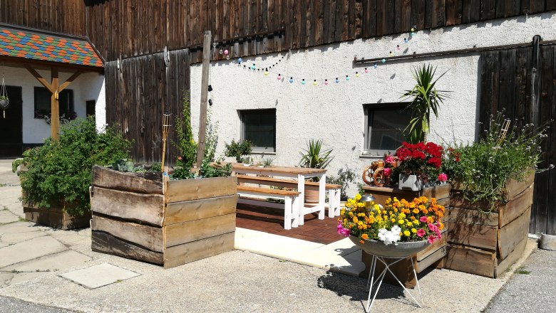 A courtyard with wooden benches, flower boxes and colorful fairy lights.