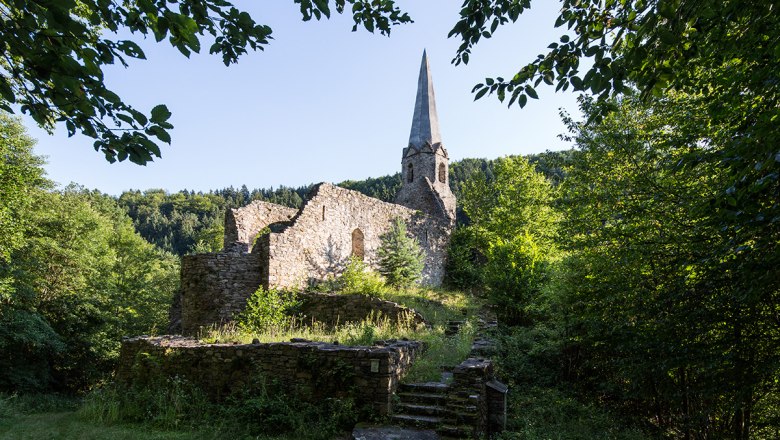 Ruins of an old church with a tower surrounded by trees.