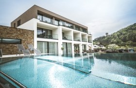 Modernes Boutiquehotel mit Pool und Liegestühlen, umgeben von grüner Landschaft.