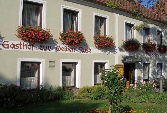 Fassade eines Gasthofs mit Blumen und Schriftzug 'Gasthof zur Weißen Rose'.