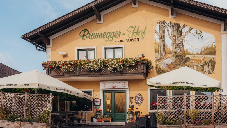 Ein traditionelles Gasthaus mit Balkon und Wandgem&auml;lde, umgeben von Sonnenschirmen und Pflanzen.