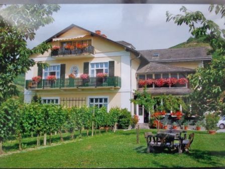 Ein zweistöckiges Haus mit Balkonen und blühenden Blumen, umgeben von einem gepflegten Garten und Weinreben.
