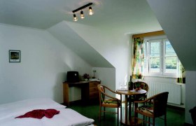 Gemütliches Zimmer mit Doppelbett, Tisch und Stühlen, Fenster mit Blick auf grüne Landschaft.