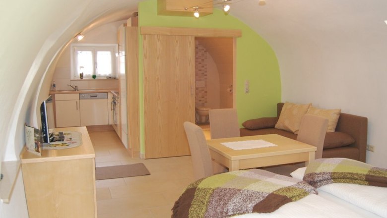 Gemütliches Apartment mit gewölbter Decke, Küche, Esstisch, Sofa und Bett.