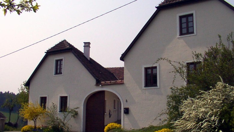 A white country house with a brown roof and garden.