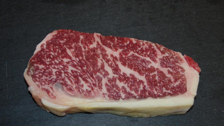 A piece of Wagyu beef with strong marbling on a black background.