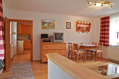 Gemütliches Wohnzimmer mit Holzmöbeln, Esstisch, Fernseher und roten Vorhängen.