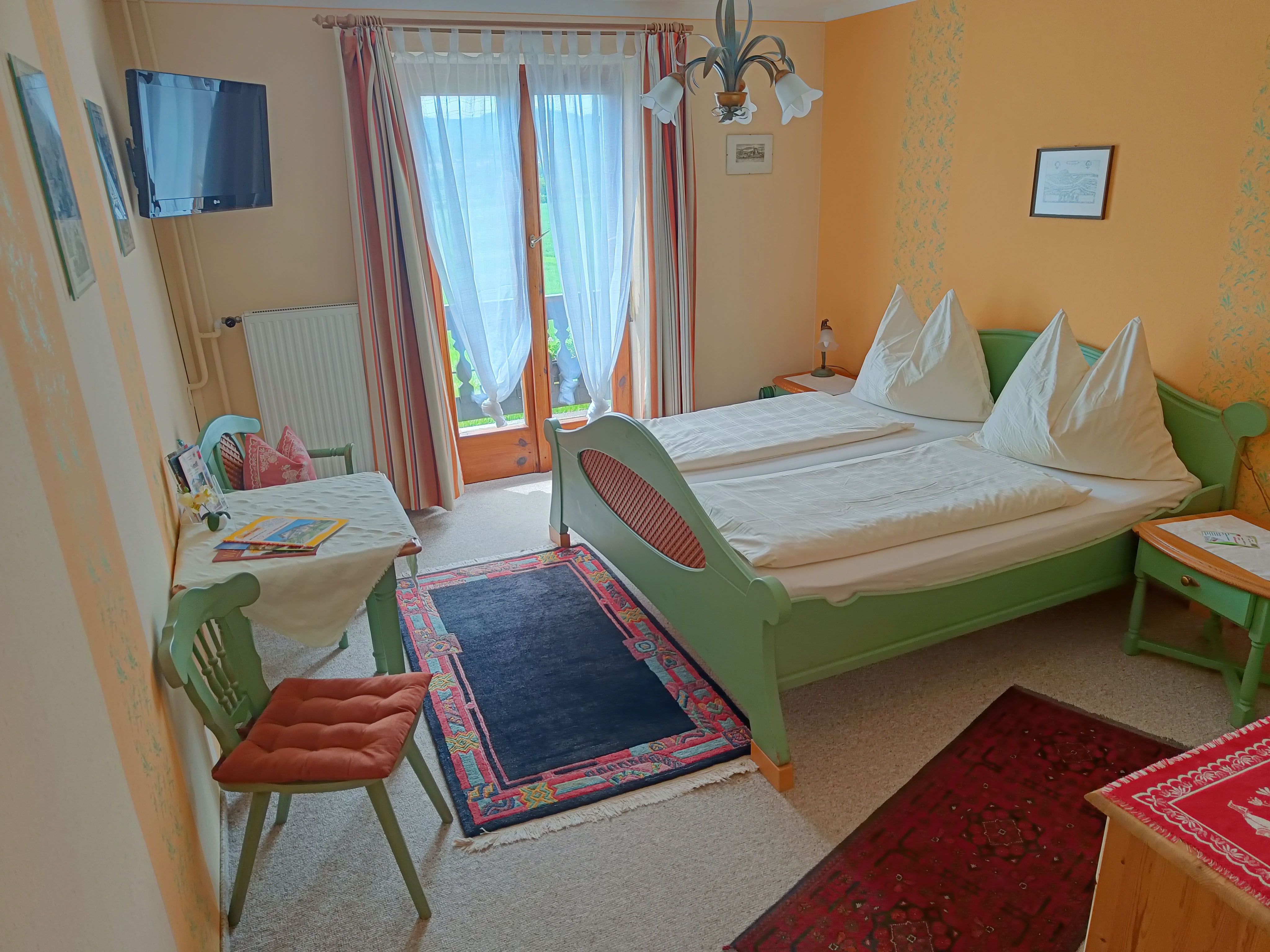 Zimmer mit grünem Doppelbett und Tisch mit Stuhl