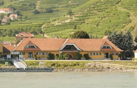 Gelbes Geb&auml;ude mit rotem Dach vor Weinbergen in Spitz an der Donau.