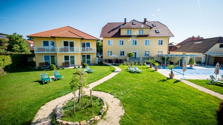 Gartenanlage mit gelben Gebäuden und Liegestühlen bei sonnigem Wetter.