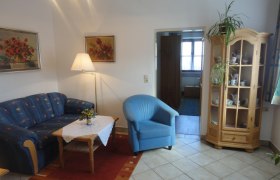 Wohnzimmer mit blauer Couch, blauem Sessel, Holztisch und Vitrine.