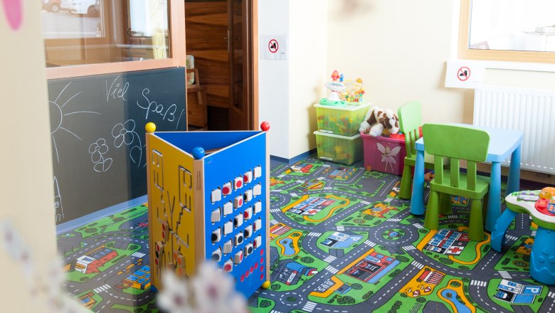 Ein bunter Kinderspielraum mit Teppich, Spielzeug und kleinen Möbeln.