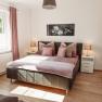Bright bedroom with double bed, two bedside tables and a window with pink curtains.