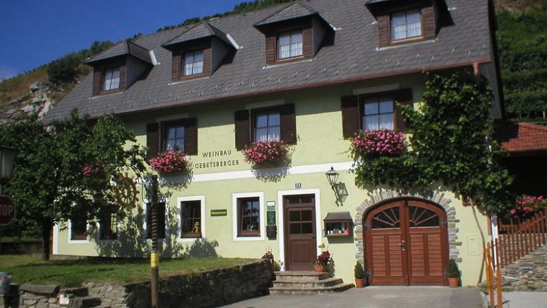 Außenansicht eines Weinguts mit gelber Fassade und Blumen.