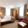 Modern hotel room with double bed, sofa, wardrobe and TV.
