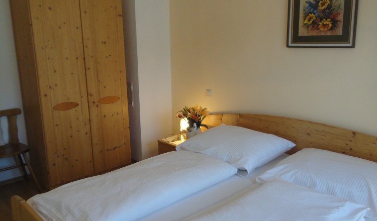 Ein gemütliches Schlafzimmer mit Doppelbett, Holzschrank, Nachttisch mit Blumen und einem Gemälde an der Wand.