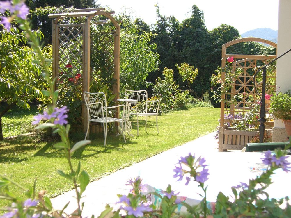 Ein sonniger Garten mit weißen Metallstühlen, einem Tisch und blühenden Pflanzen.