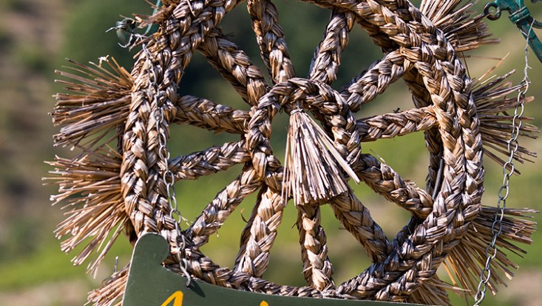 A woven straw wreath with the sign 'Ausg'steckt is!' hangs on a chain.