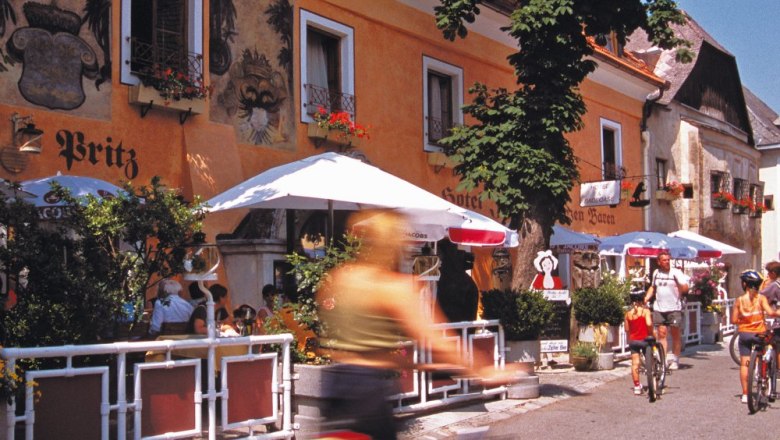 Radfahrer vor einem Hotel mit Terrasse und Sonnenschirmen.