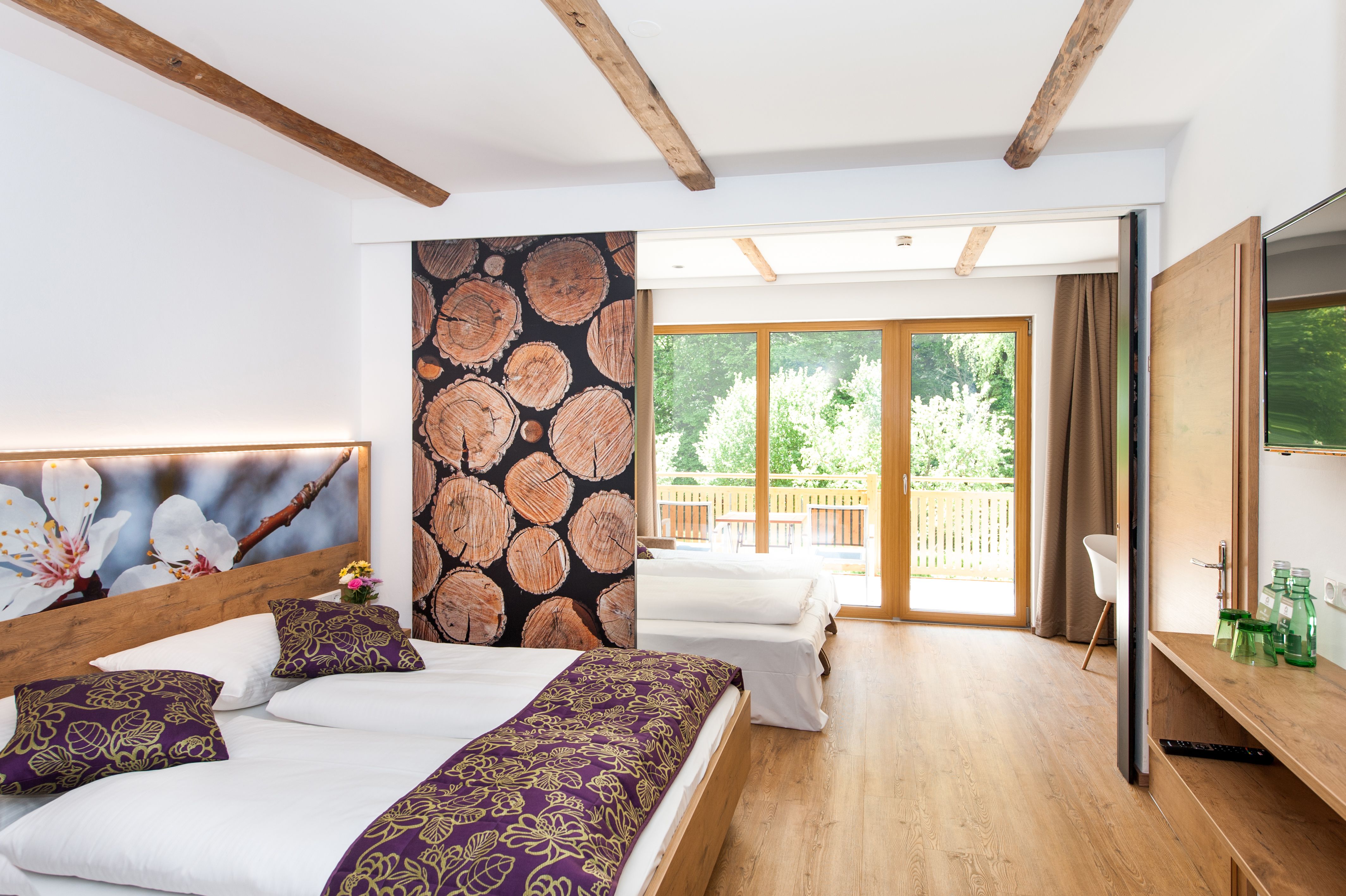 Ein modernes Familienzimmer mit Holzboden, zwei Betten, großen Fenstern und dekorativen Holzelementen.