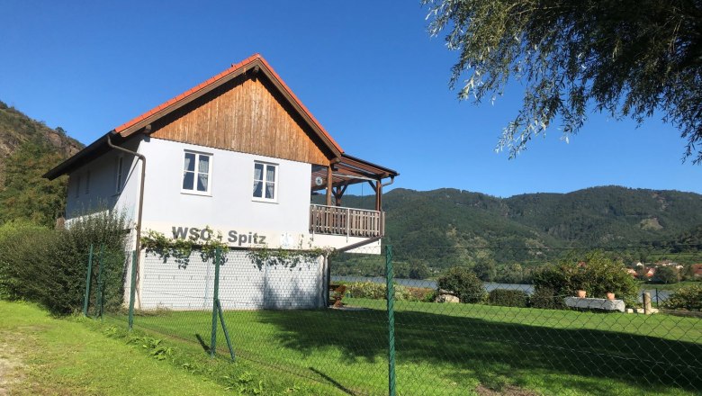 A clubhouse with the inscription 'WSC Spitz' in front of a mountain landscape.