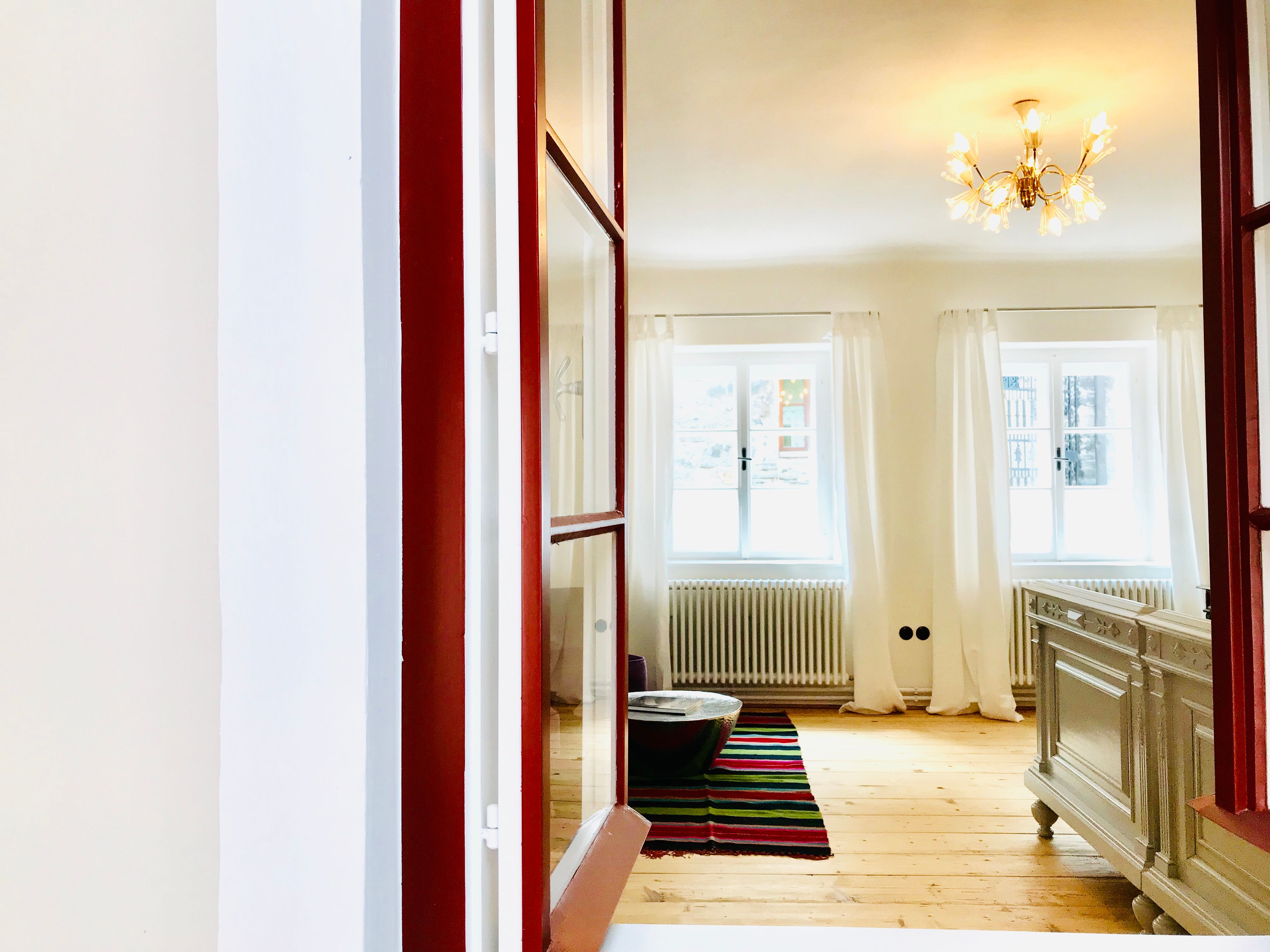 Helles Schlafzimmer mit Holzboden, weißen Vorhängen und einem Kronleuchter.