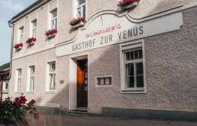 Gasthof zur Venus mit blumengeschmückter Fassade und Holztür.