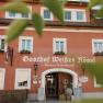 Facade of the Wei&szlig;es R&ouml;ssl inn in M&uuml;hldorf with red wall and white windows.