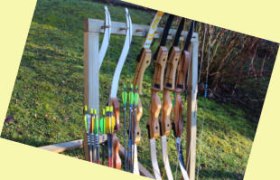 A stand with several bows and arrows on a meadow.