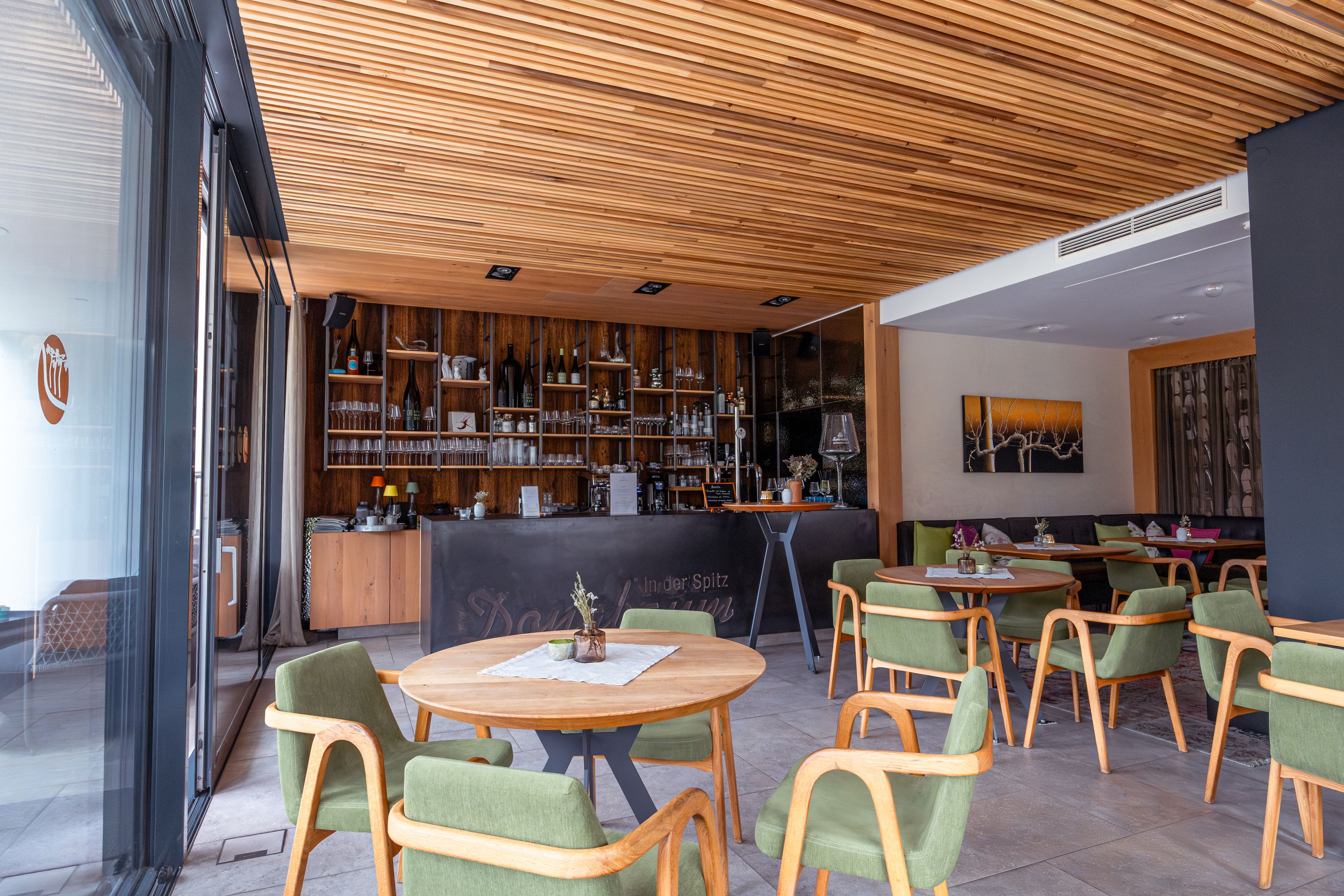Innenansicht der Weinlounge mit Holzelementen, grünen Stühlen und einer Bar im Hintergrund.