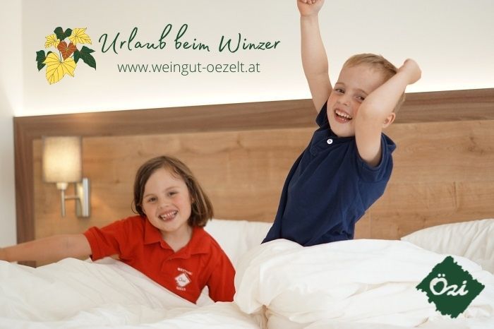 Zwei Kinder spielen fröhlich in einem Bett in einem Gästezimmer.