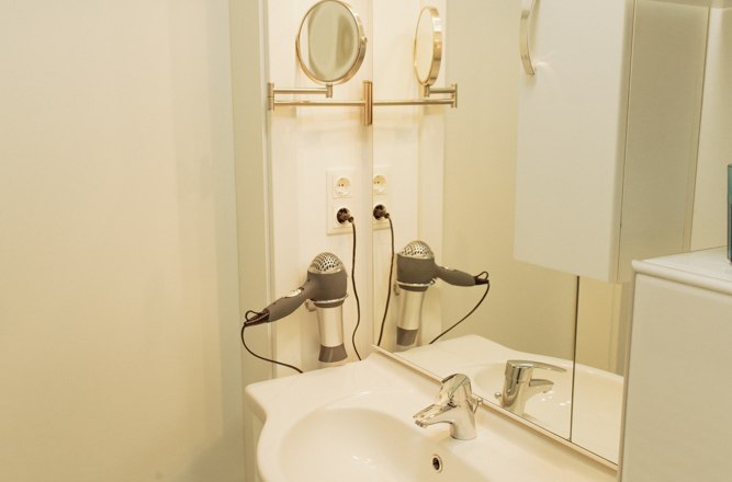 Modern bathroom with washbasin, mirror, hairdryer and white cupboards.