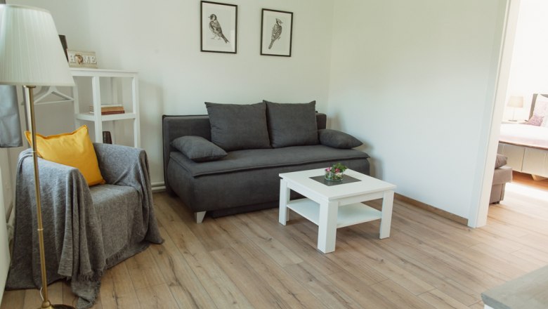 Modern living room with gray sofa, armchair, white coffee table and wooden floor.