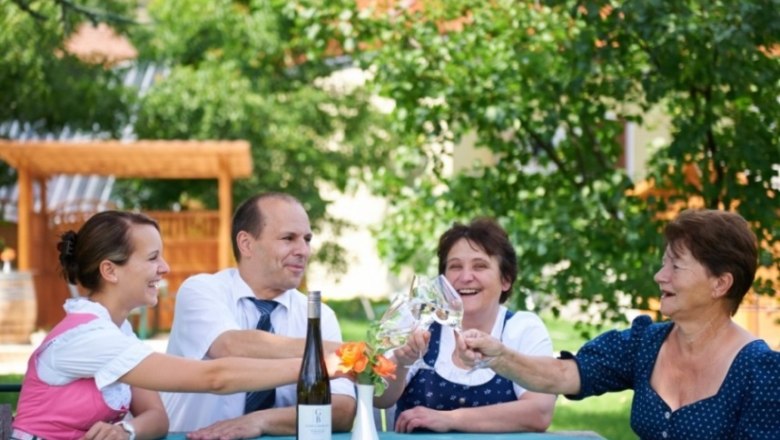 Four people clink glasses of wine at a table outside.