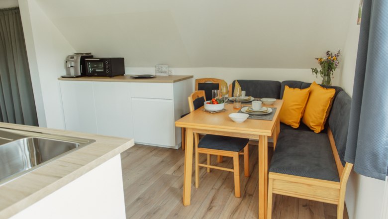 Cozy dining area in a modern apartment with wooden table, corner bench and yellow cushions.