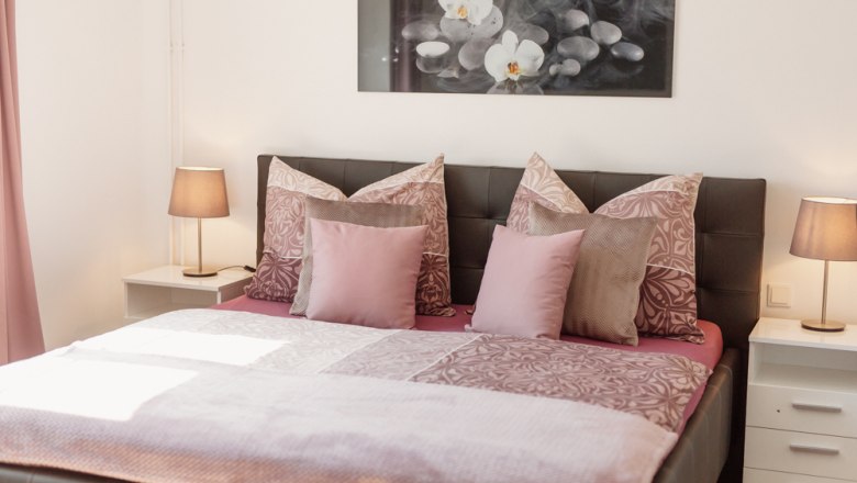 Cozy bedroom with double bed, pink bed linen and two bedside tables with lamps.