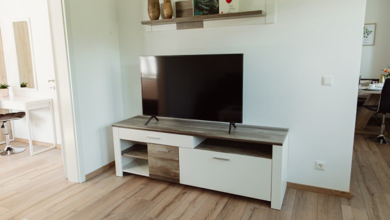 Living room with TV on a white TV cabinet, above a shelf with decorations.