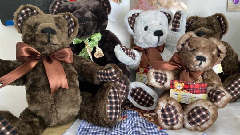 Fünf Plüschbären mit Schleifen sitzen auf einem Tisch.