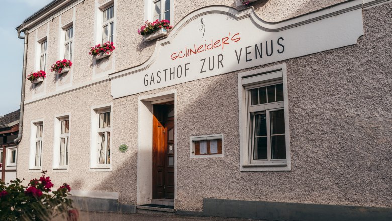 Wirtshaus in Willendorf, © Niederösterreich Werbung/Daniela Führer Gasthof zur Venus mit blumengeschmückter Fassade und Holztür.