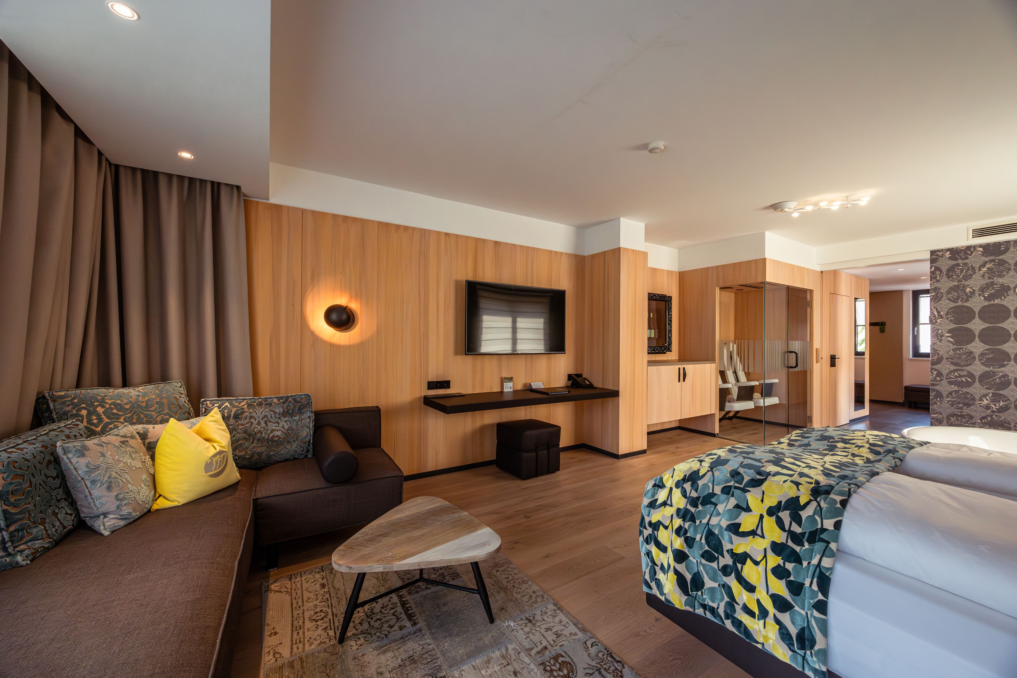 Modernes Hotelzimmer mit Holzverkleidung, Sofa, Bett und Flachbildfernseher.