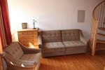A living room with a sofa, an armchair, a chest of drawers and a spiral staircase.