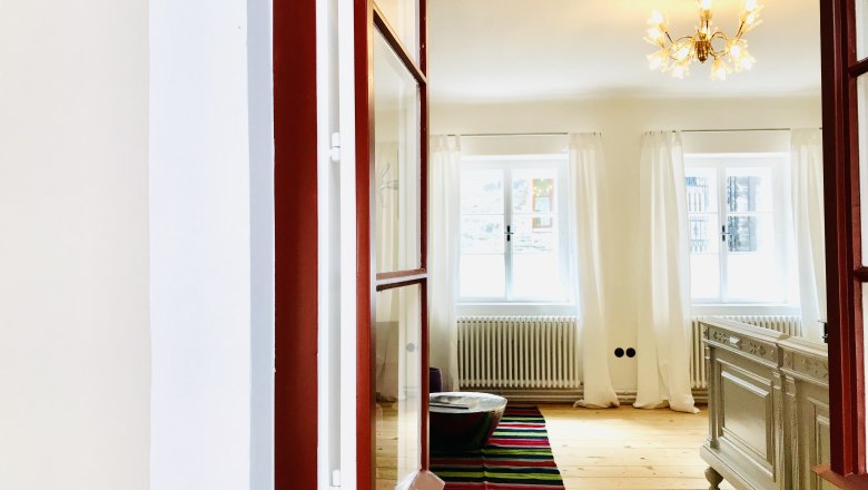 Helles Schlafzimmer mit Holzboden, weißen Vorhängen und einem Kronleuchter.