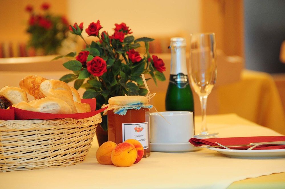 Frühstückstisch mit Brötchenkorb, Marmelade, Sektflasche und Rosen.