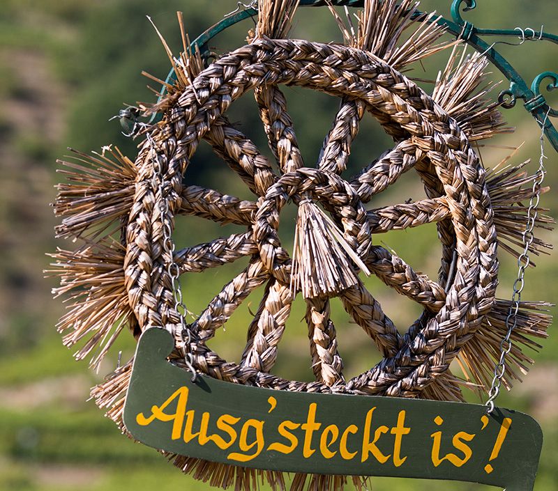 Strohkranz mit Schild 'Ausg'steckt is'' vor unscharfem Hintergrund.