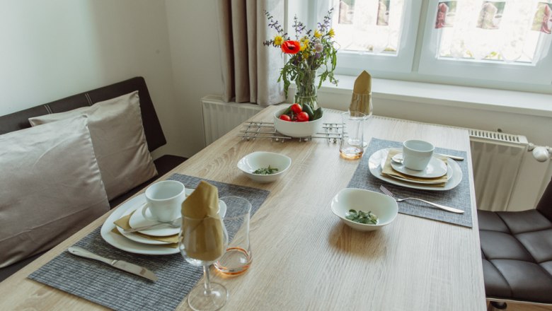 A dining table set with crockery, glasses and flowers in a bright room.