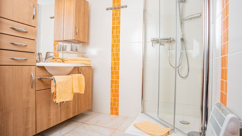Modernes Badezimmer mit Holzm&ouml;beln, Dusche und orangefarbenen Akzenten.