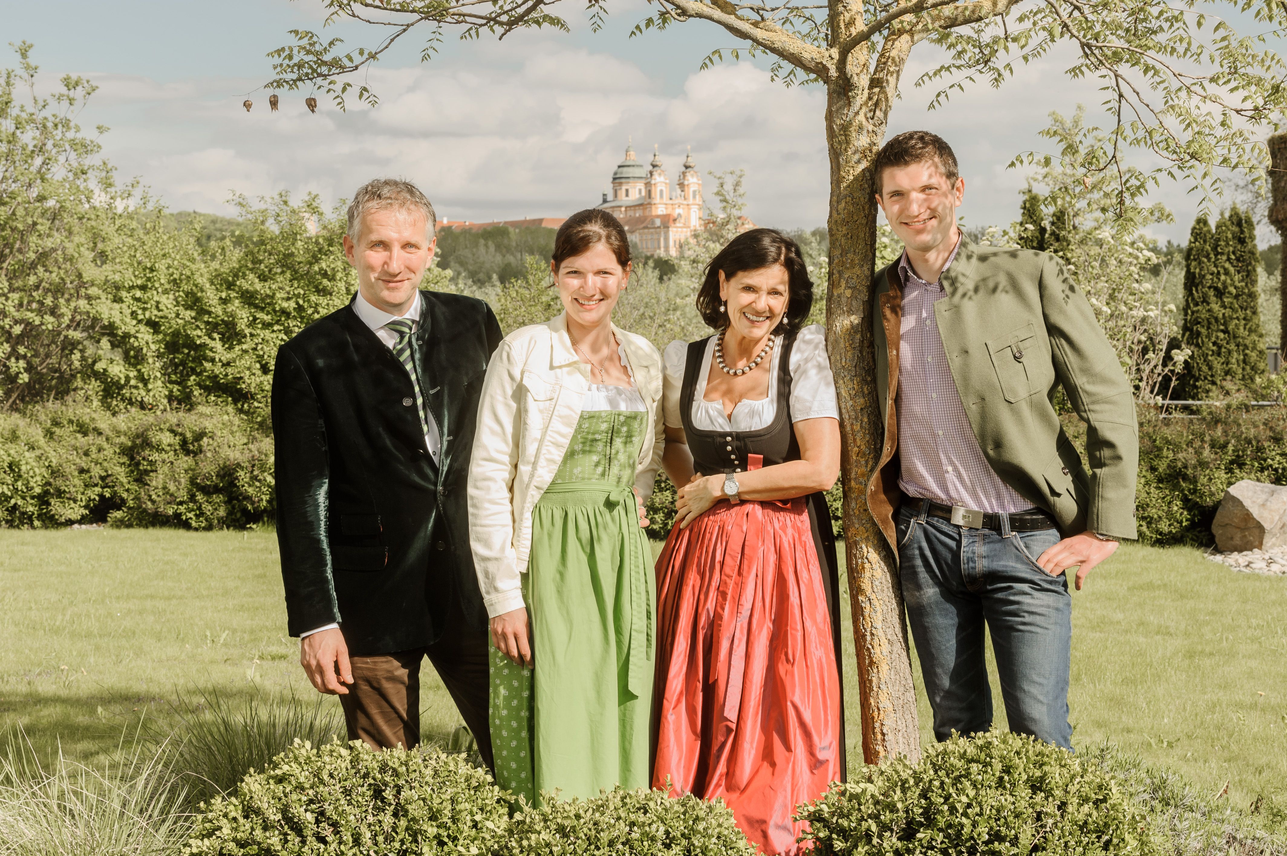 Familie Pichler  in traditioneller Kleidung stehen im Freien vor einem Baum, im Hintergrund ist Sift Melk zu sehen