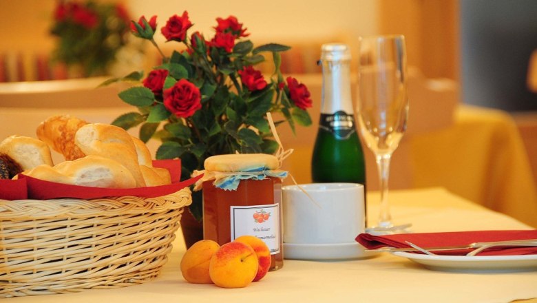 Frühstückstisch mit Brötchenkorb, Marmelade, Sektflasche und Rosen.