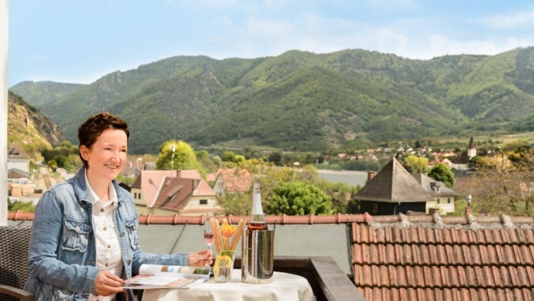 Frau auf Balkon mit Blick auf Berge und Dorf.