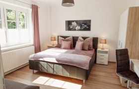 Bright bedroom with double bed, two bedside tables and a window with pink curtains.